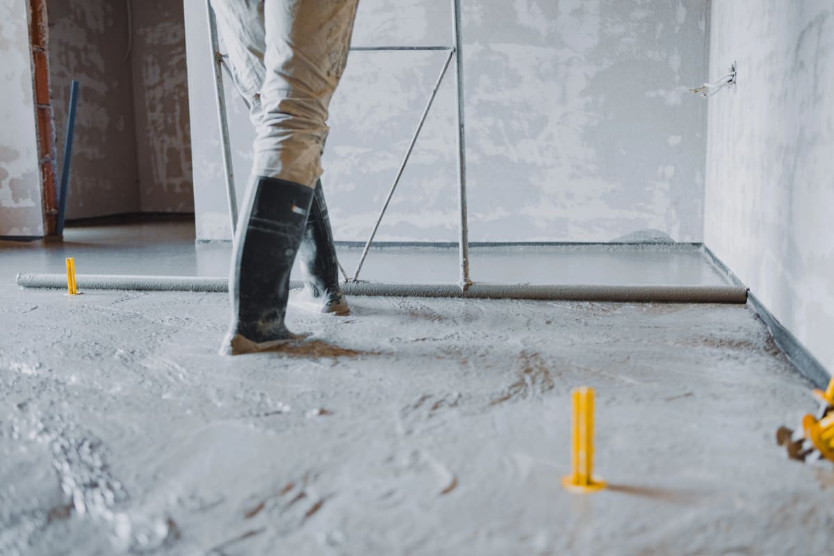 Estrichleger glättet Fließestrich mit Abziehlatte - Höhenpunkte für perfekte Ebenheit