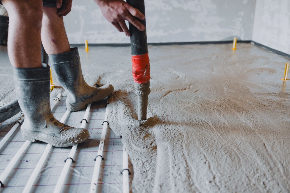 Estrichleger pumpt Fließestrich auf Tackerplatte mit Heizrohren - Nahaufnahme Einbau