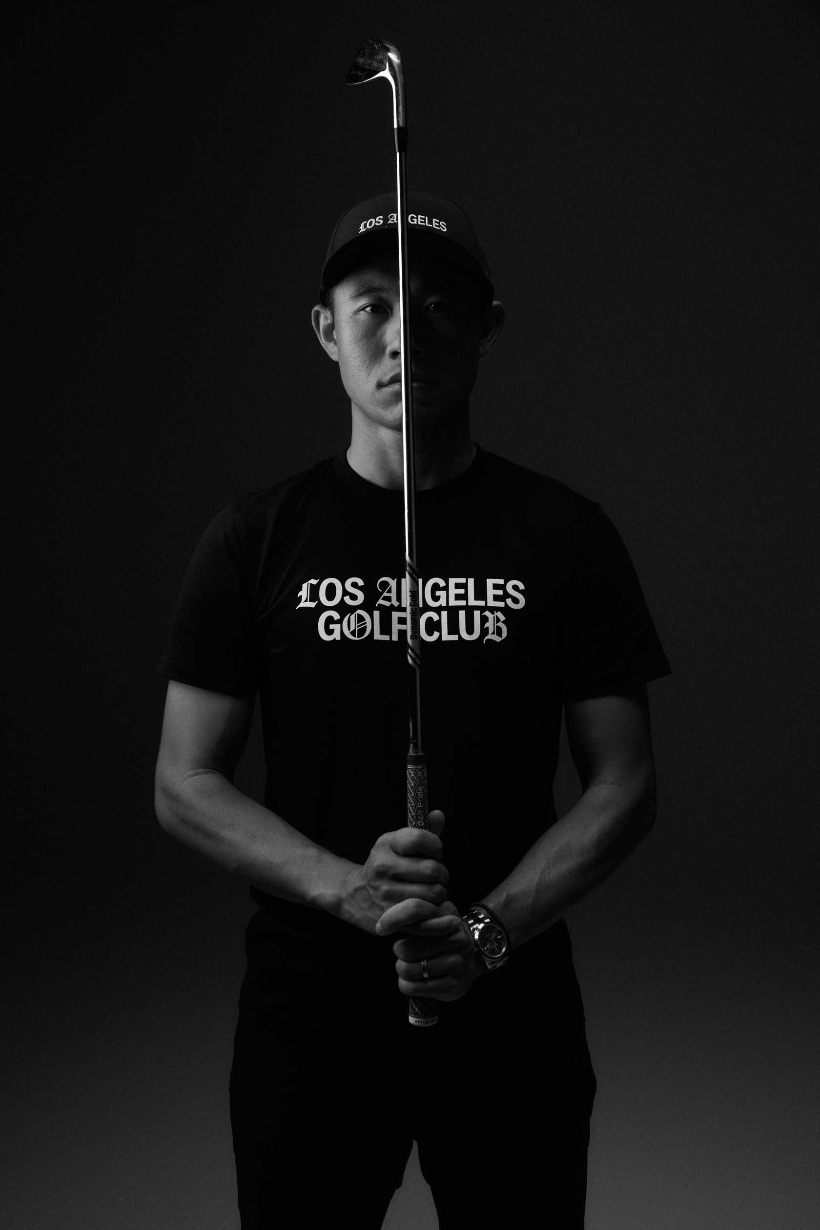 Collin Morikawa wearing a black t-shirt stands with a golf club during the photo shoot
