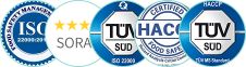 خمس شعارات في صف تعرض الشهادات: ISO 22000:2018، SORA، TÜV SÜD ISO 22000، HACCP، وTÜV SÜD. كل شعار فيه على اللون الأزرق وعناصر تصميم دائرية.