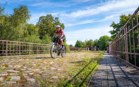 Kelly leads the charge across an old cobblestone bridge as other riders follow suit-