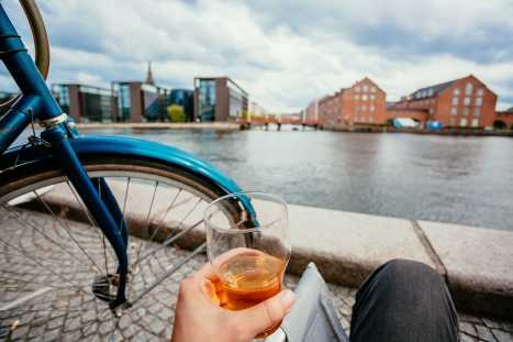 Lonely person drinking beer outdoor, past river and cityscape of Copenhagen. Social distance and lifestyles concept