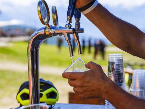 Hands of man pour beer into a plastic cup, in the mountains, in the Aosta Valley