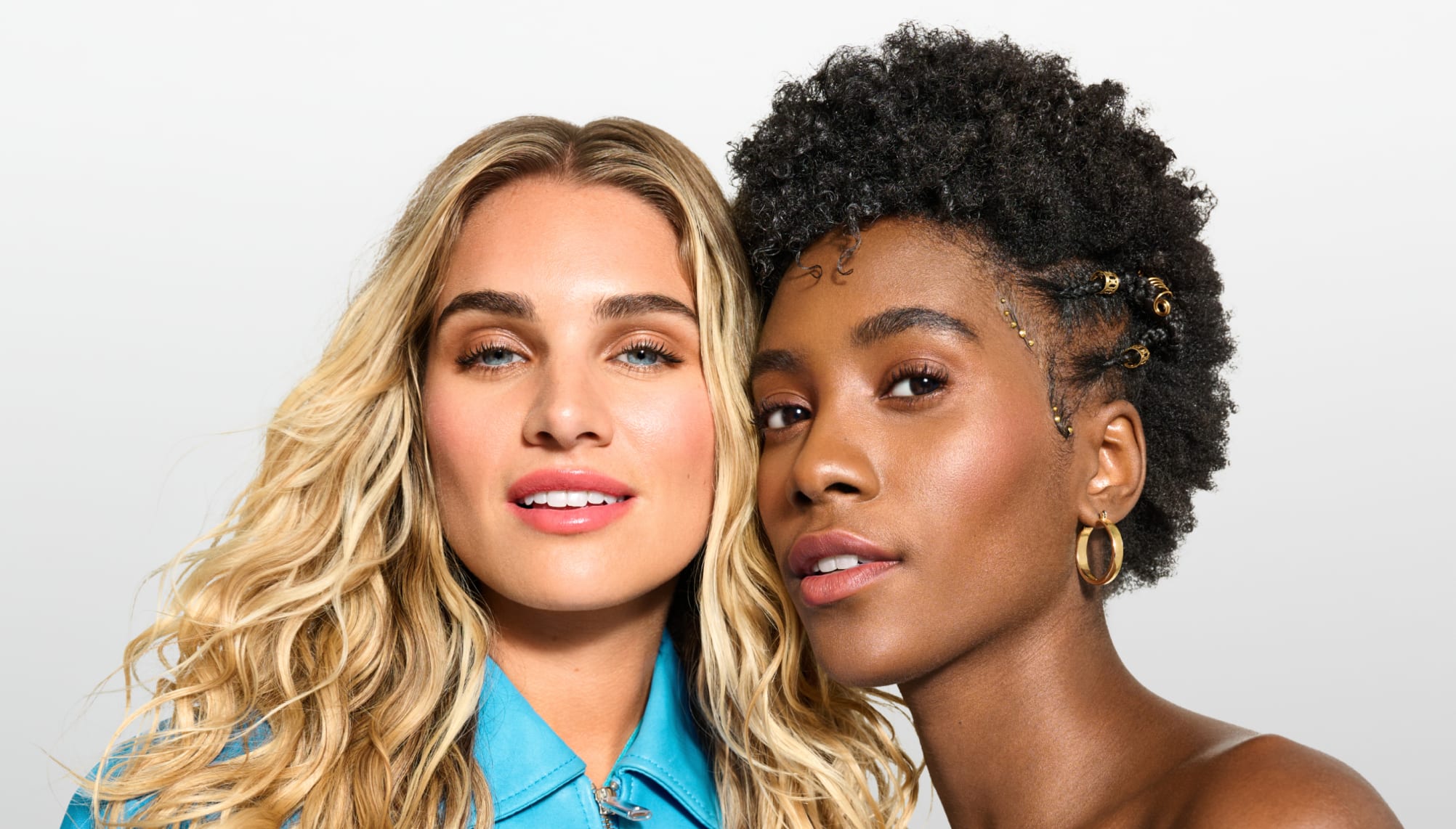 two women: one with long blonde wavy hair and the other with short brown coily hair