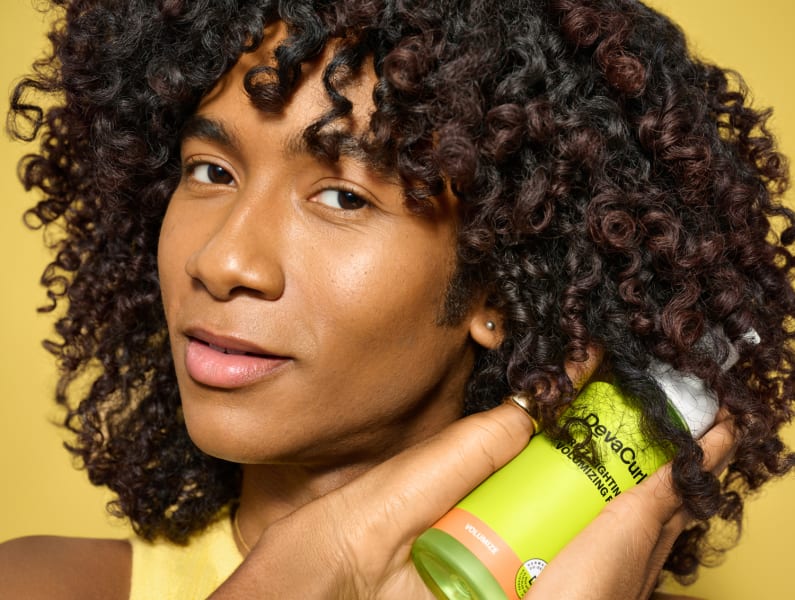 person with curly hair holding Frizz-Fighting Volumizing Foam