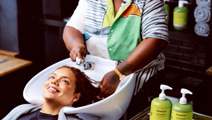 woman at the sink smiling while stylist wets curls