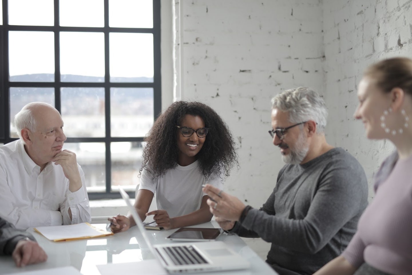 A group of professionals in a mixture of casual and work attire sit around a desk, apparently enjoying a positive discussion.