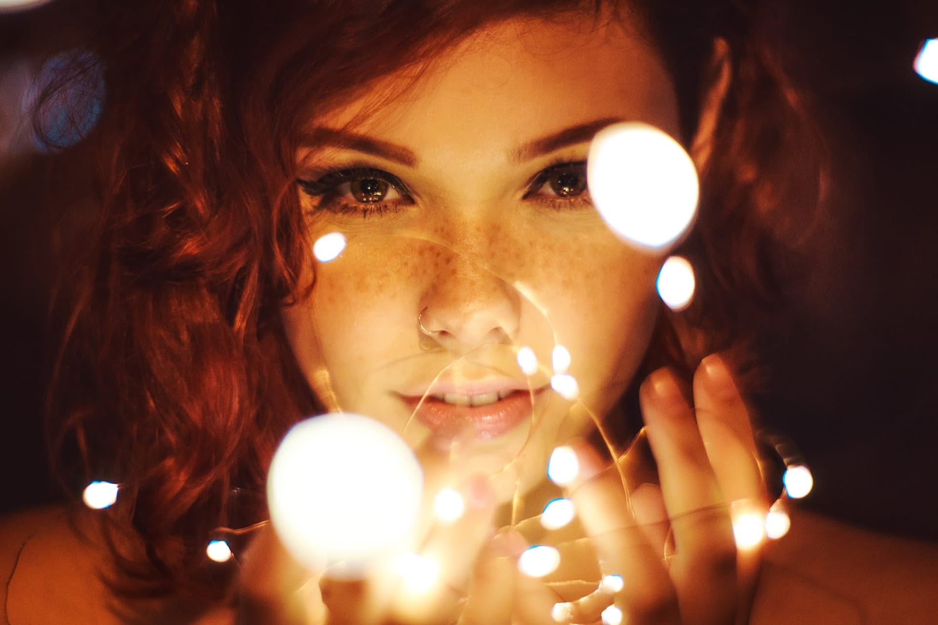 A young woman gazes mysteriously at us through a series of lights held in her fingers