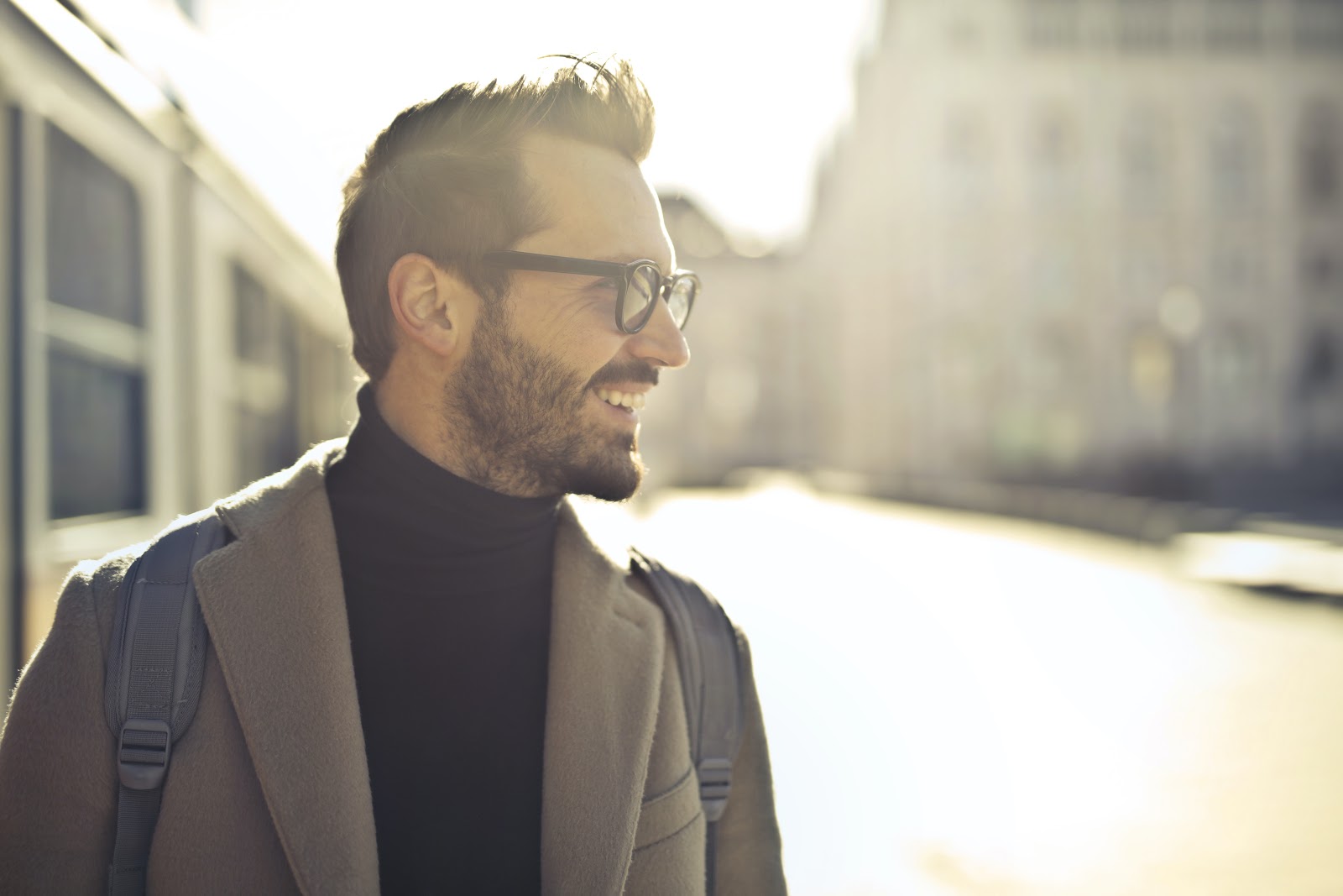 A photograph of a confident man in smart clothes wearing a backpack and walking down a city street during the golden hour.