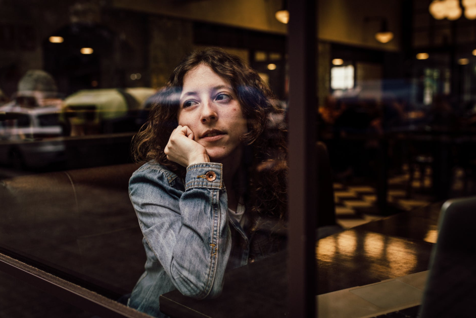 A woman in a denim jacket stares longingly out of a window.