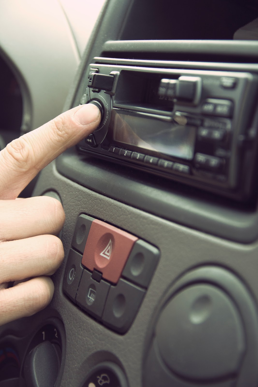 A close up of a driver's hand reaching towards an in-car stereo featuring a cassette player.
