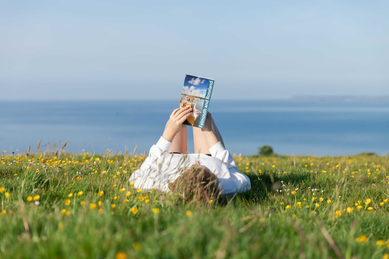 Woman laying on back in grass reading Friendly Guide Book