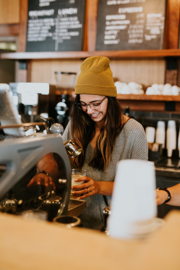 Young woman smiling making coffee in cafe