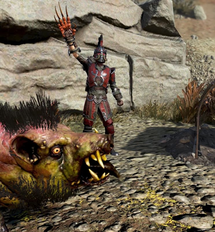 A Fallout 76 character wearing spiked red armor and a gladiator-style helmet stands on rocky ground, raising a clawed weapon in one hand. In the foreground, a mutated creature resembling a boar with pink and green mottled skin, sharp tusks, and a black mane snarls aggressively. To the right is a curved metal shelter frame, and behind them are large stone boulders under a bright sky.