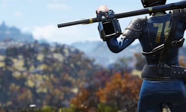 A Fallout 76 character in a blue jumpsuit with '76' on the back stands on a rocky ledge, holding a rifle. They're wearing a helmet and armor, with mountains and autumn trees in the background. A 'Vault 76' sign is visible in the lower left corner
