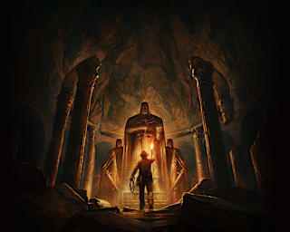 Indiana Jones holding a torch up to a large statue inside a cavern.