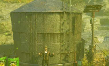 An image from Fallout 76 featuring a Weather Control Station (Blooming Haze) emitting green haze, a Poisoned Earth Well with toxic barrels nearby, a large Steel Silo in the center, and a Mulch Barrel on the right. The background shows a rocky terrain with sparse vegetation under an overcast sky
