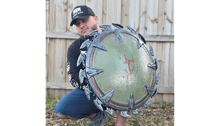 Artist GameQraft crouches behind his fabricated Shield Saw