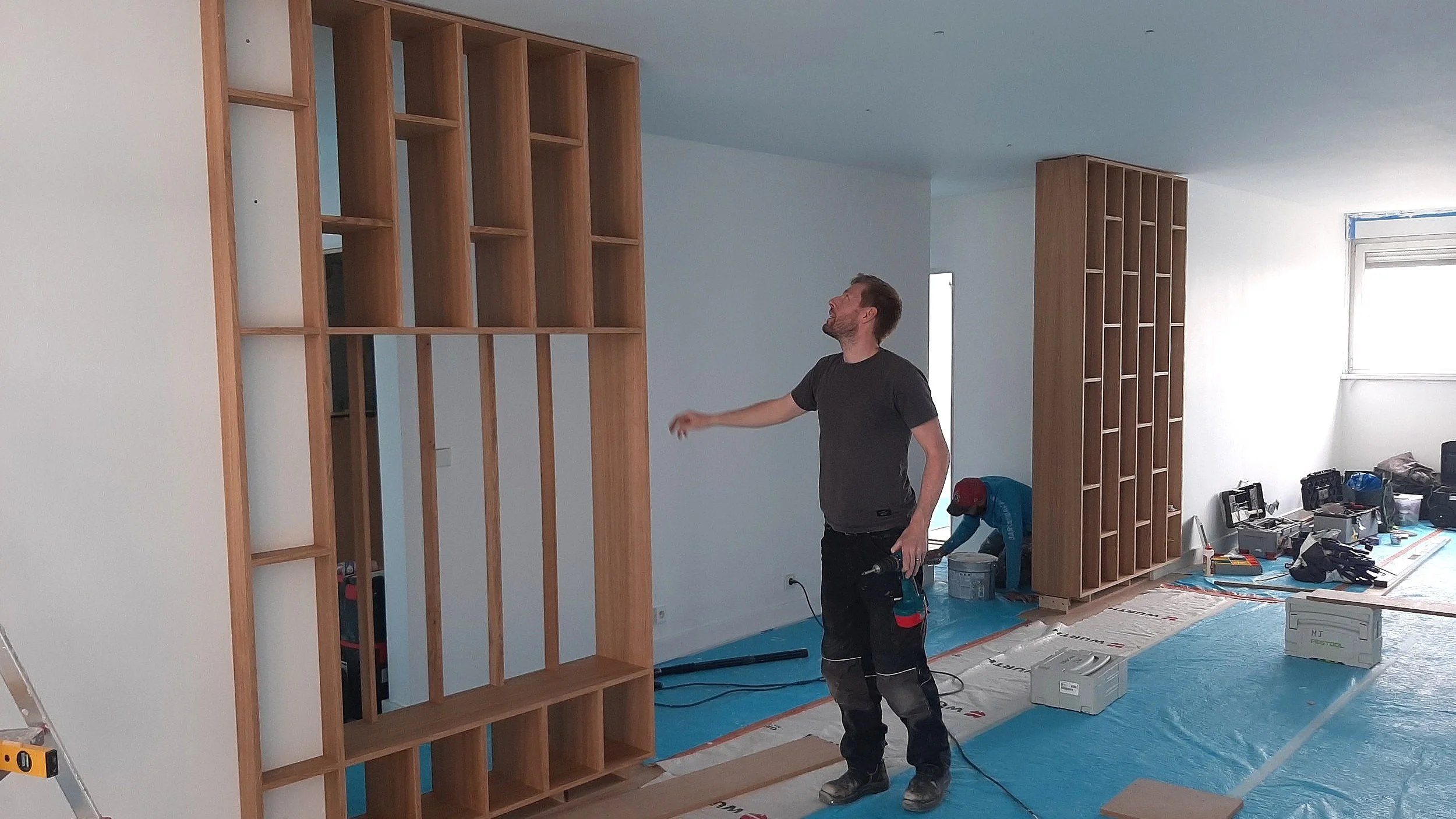 Deux hommes installent des étagères en bois dans une pièce en rénovation