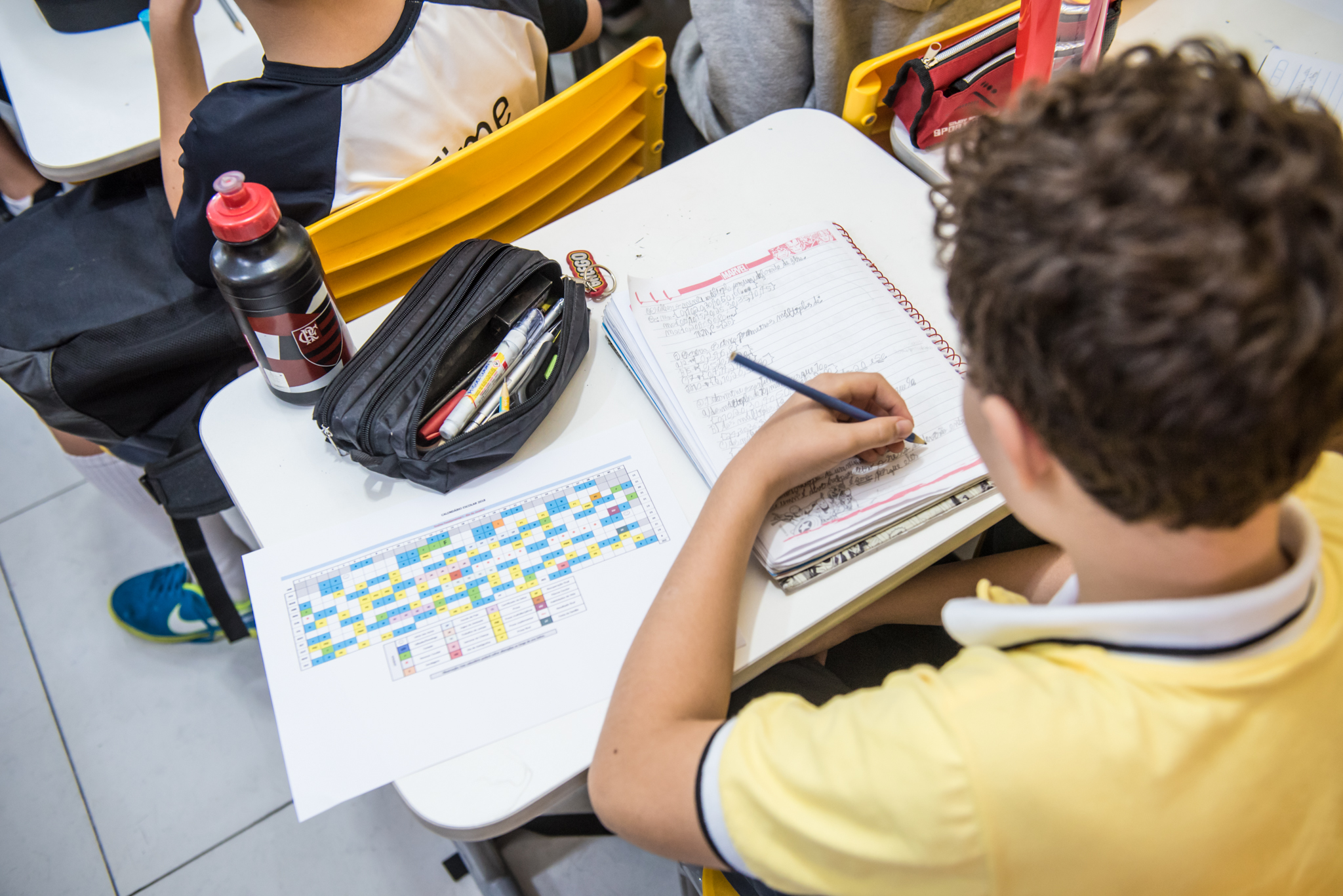 Alumno escribe en su cuaderno en el aula, con el calendario escolar sobre el pupitre