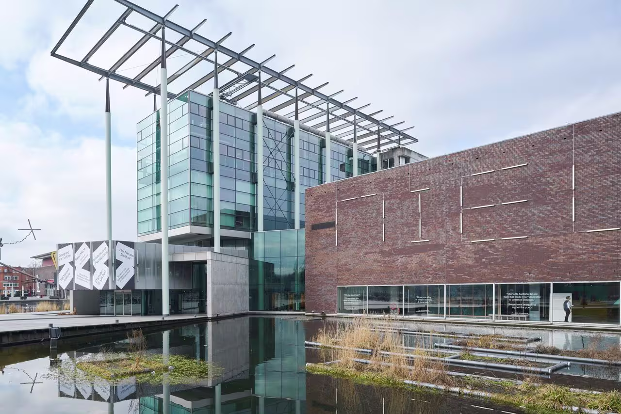 Modern gebouw van Het Nieuwe Instituut met glazen gevel en bakstenen muur, gelegen aan het water met reflectie.
