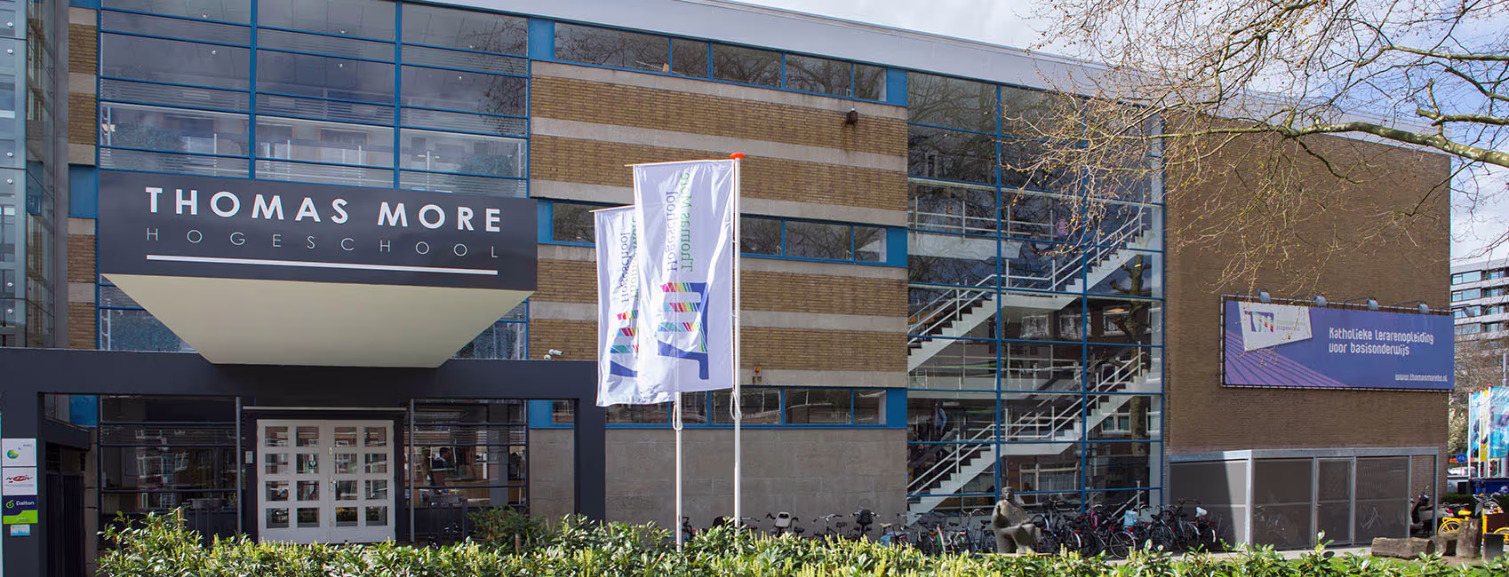 Modern schoolgebouw van Thomas More Hogeschool met glazen gevel, fietsen en studenten bij de ingang.