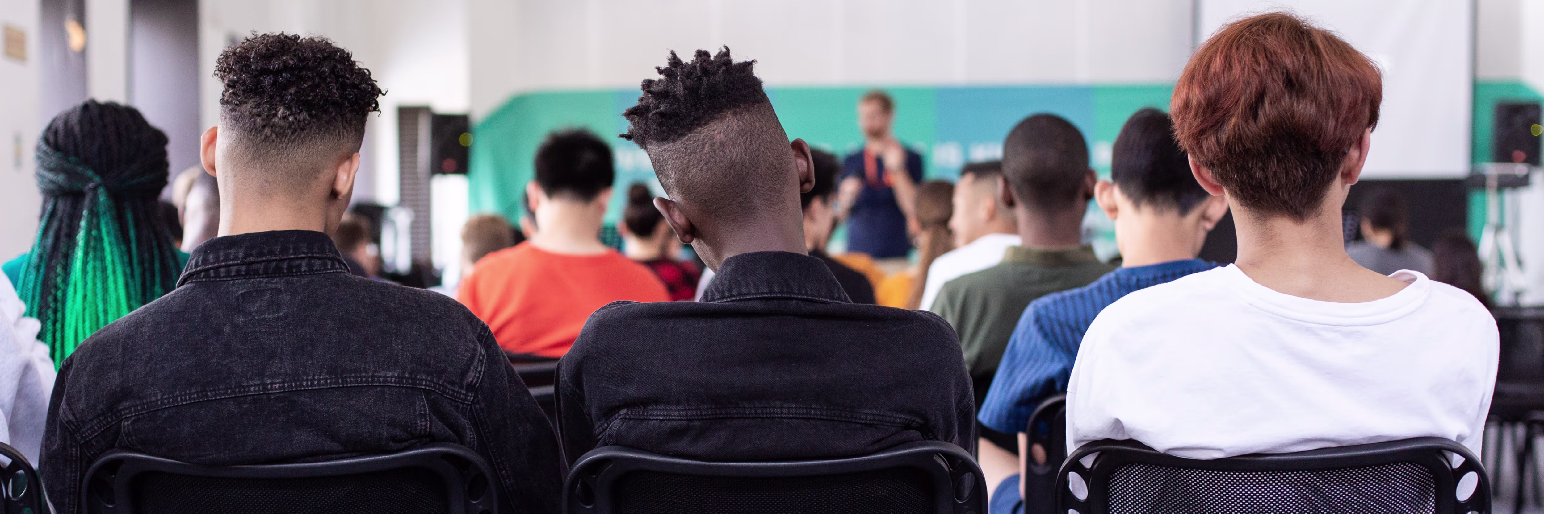 Groep mensen van achteren gezien die naar een presentatie kijken in een moderne ruimte met groene achtergrond.
