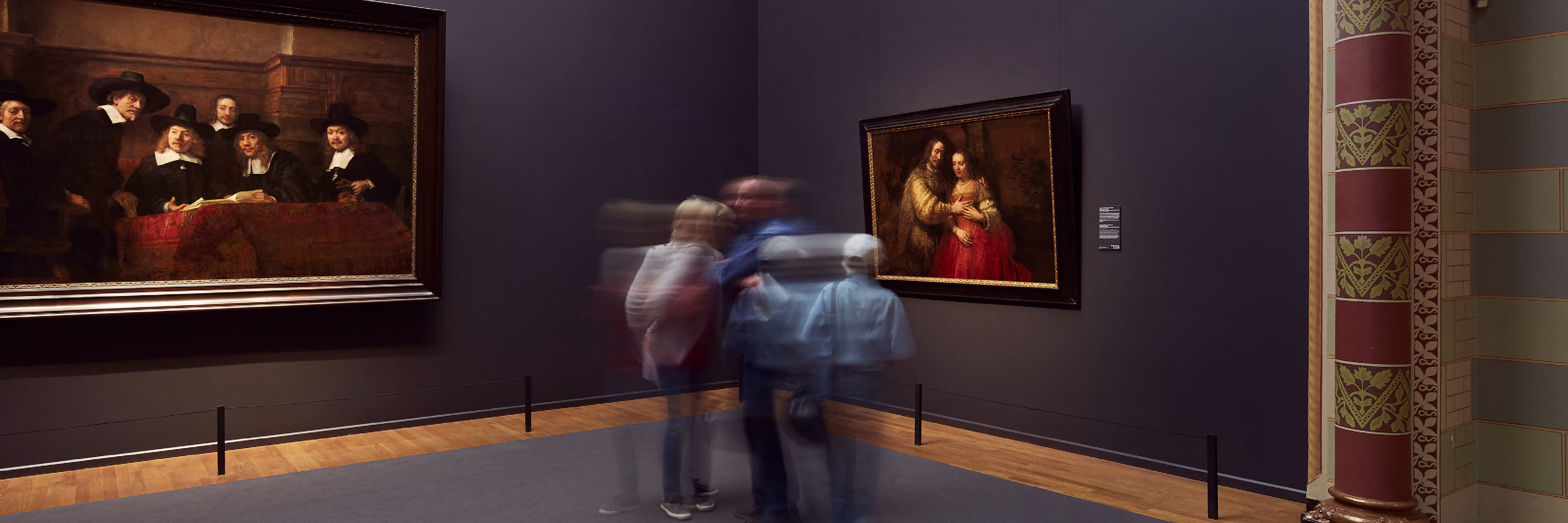 Bezoekers bekijken klassieke schilderijen in een museumzaal met paarse muren en houten vloer.