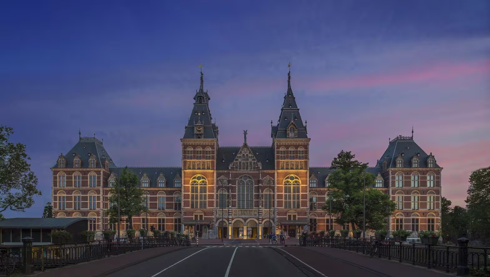 The Rijksmuseum in Amsterdam, illuminated at dusk, with its distinctive red-brick facade and towers.