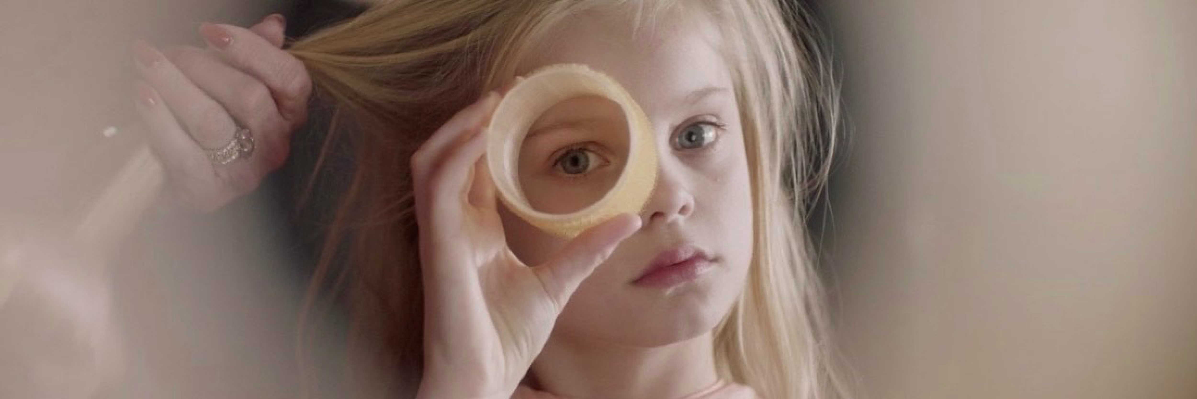Een blonde vrouw kijkt door een ronde houten ring die ze voor haar oog houdt, wat een artistiek en speels effect creëert.