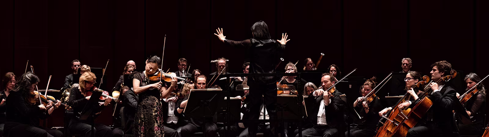 Een dirigent leidt een orkest met strijkers en andere musici tijdens een klassieke muziekuitvoering op het podium.