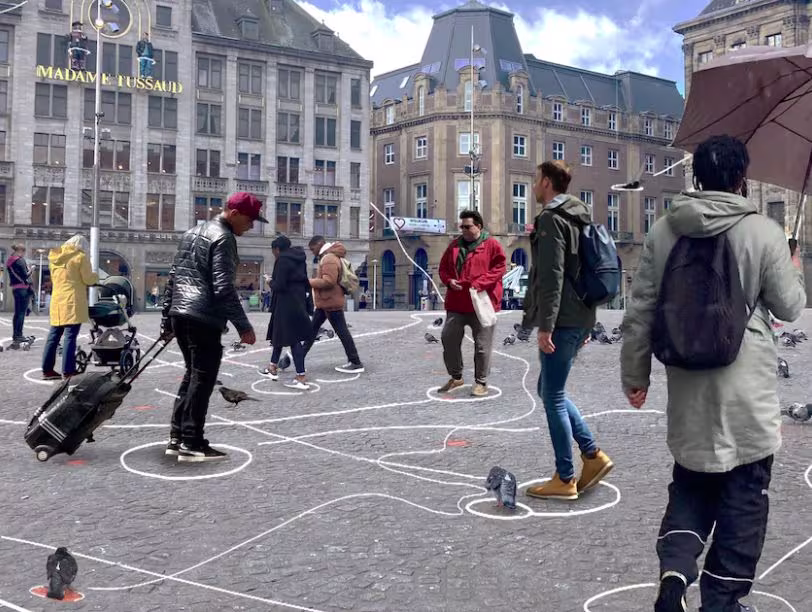 People are standing in white circles in a square in front of Madame Tussauds, likely due to COVID-19 precautions or an event.