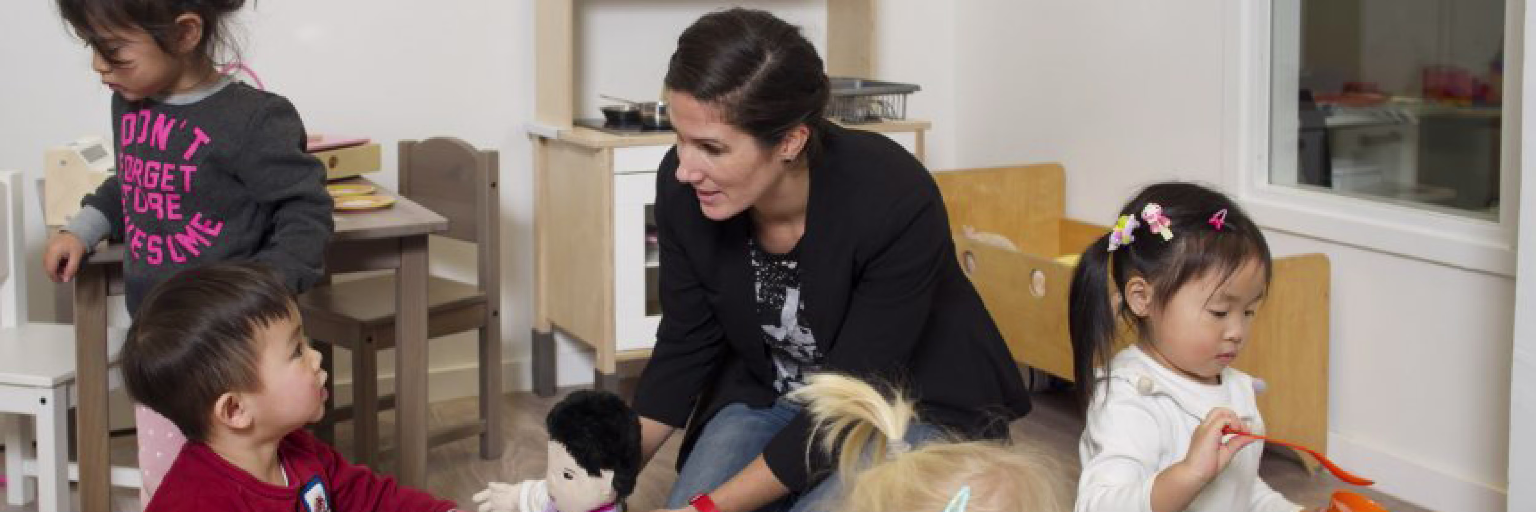 Een leidster zit op de grond en speelt met vier jonge kinderen in een kinderdagverblijf.
