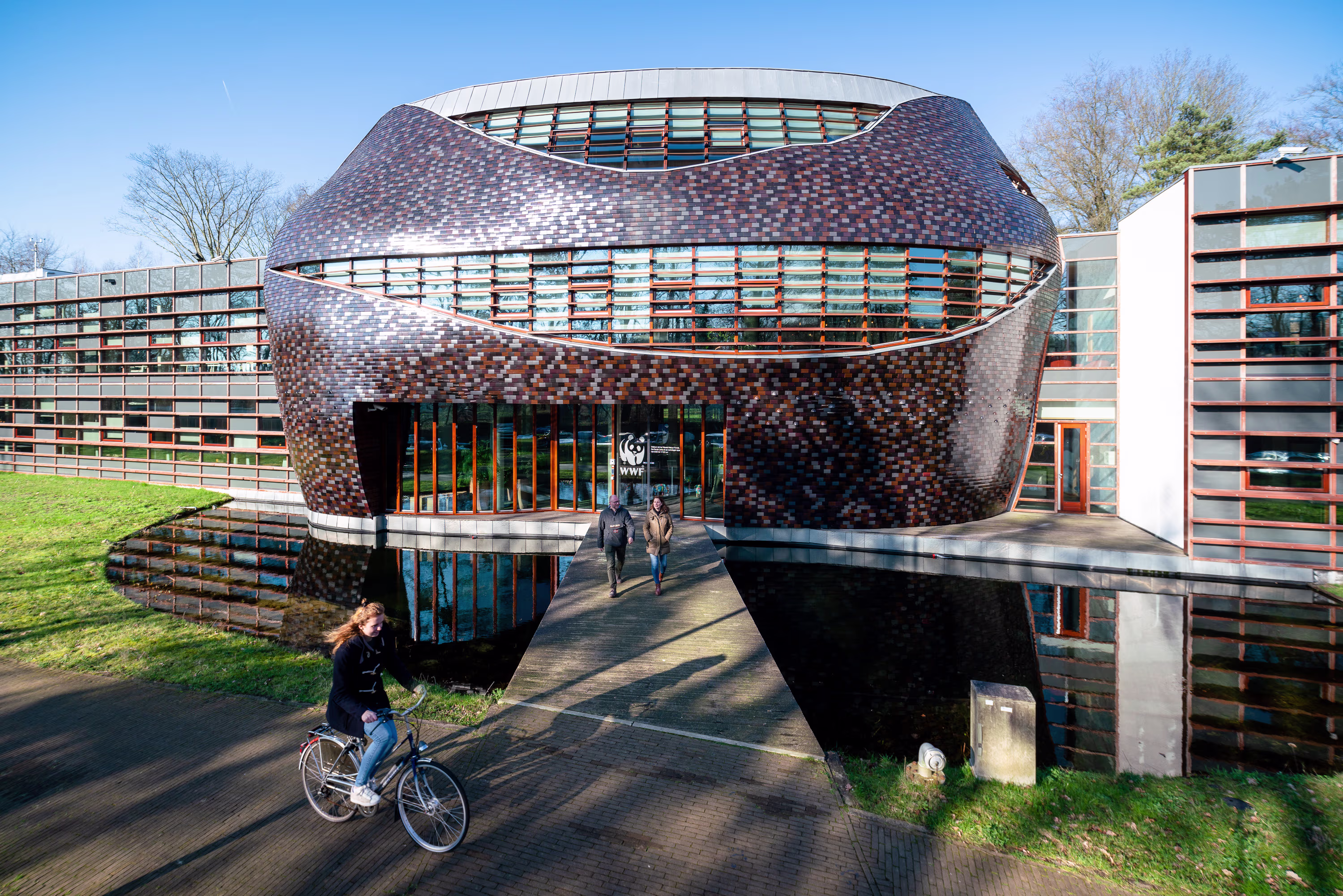 Modern WNF-gebouw met organische vormgeving en kleurrijke gevel, persoon op fiets rijdt erlangs over betonnen pad.