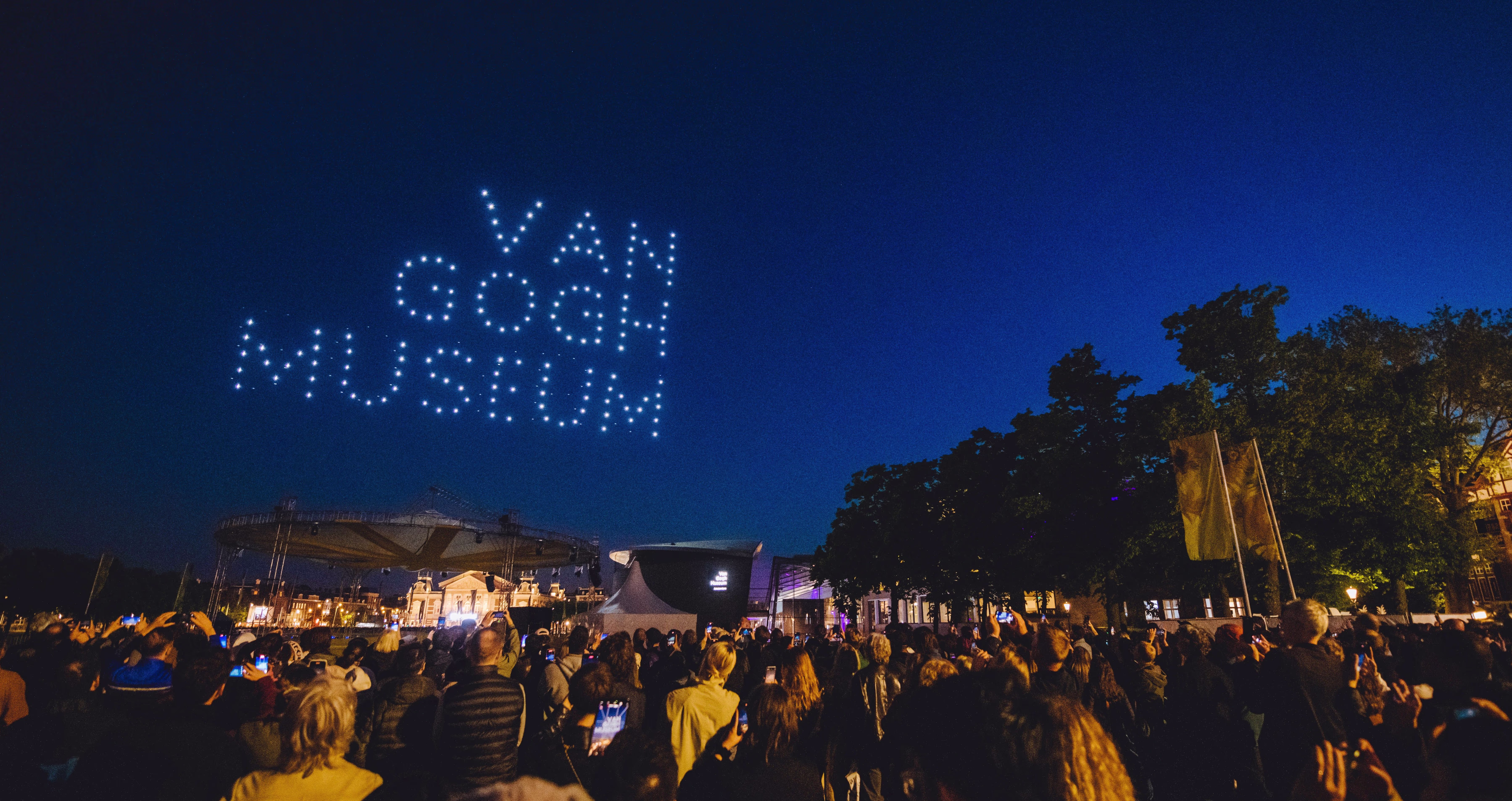 Een menigte mensen kijkt 's avonds naar een drone-lichtshow die 