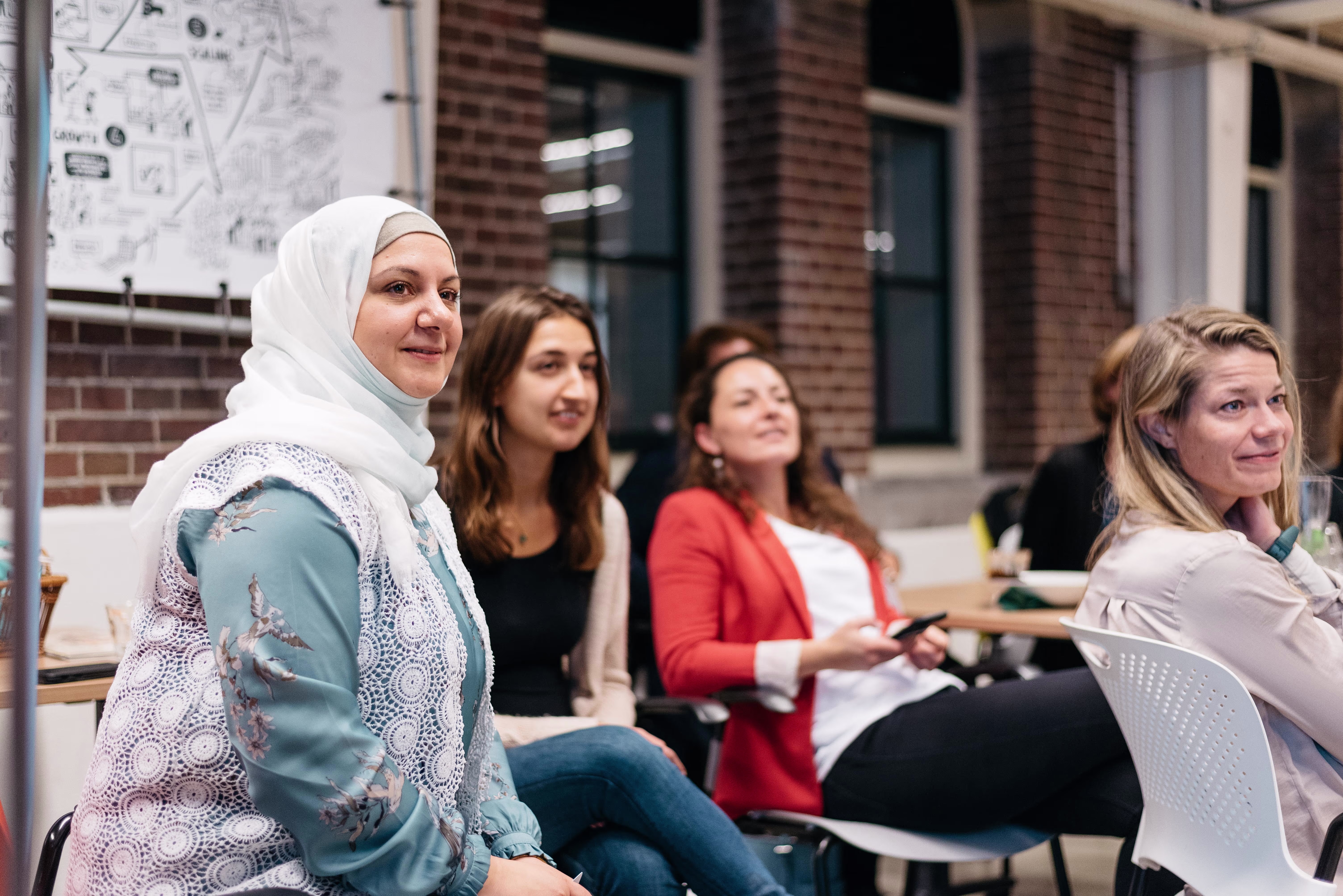 Vier vrouwen zitten lachend in een moderne kantooromgeving tijdens een bijeenkomst of training.