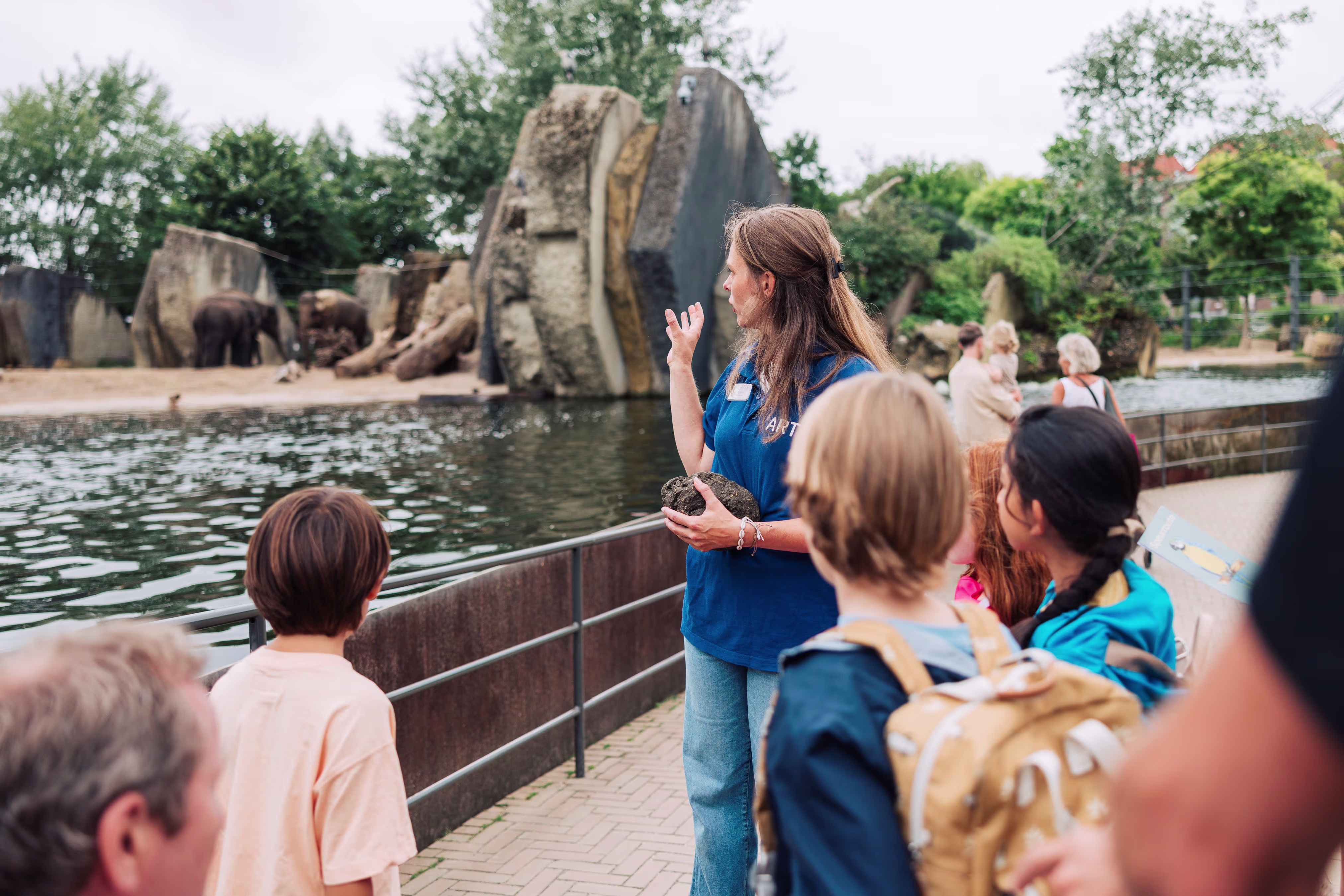 Een gids in blauw shirt geeft uitleg aan een groep bezoekers bij het olifantenverblijf in ARTIS dierentuin.