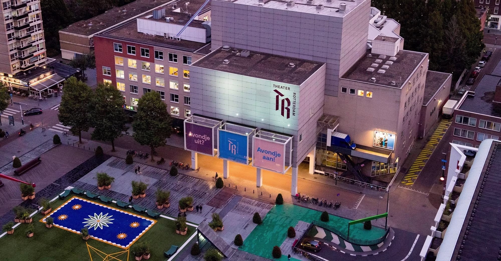 Aerial view of Theater Rotterdam at night, with its illuminated facade and colorful decorations on the forecourt.