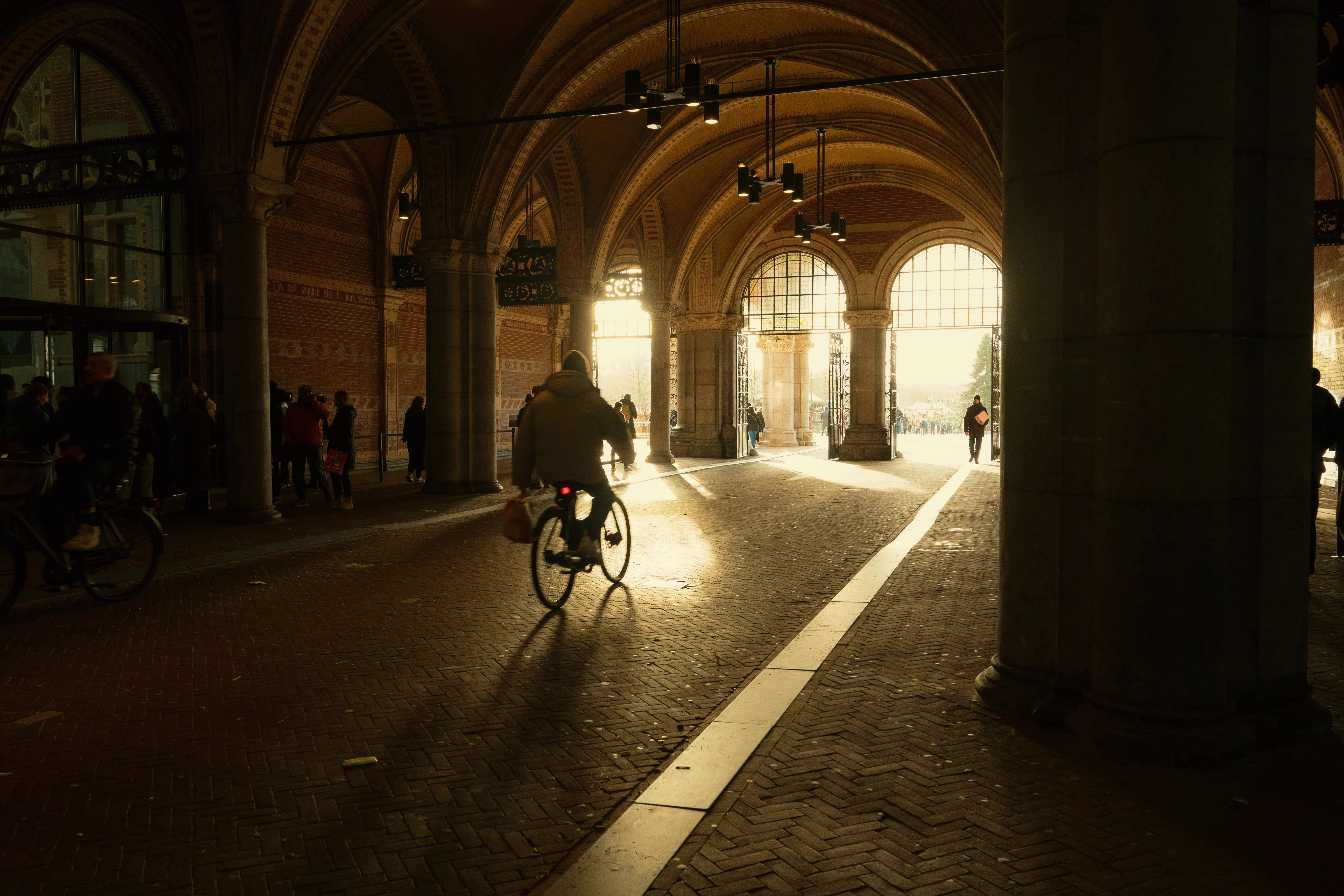 Een fietser rijdt door een historische onderdoorgang met gewelfde bogen, waar warm licht naar binnen valt.