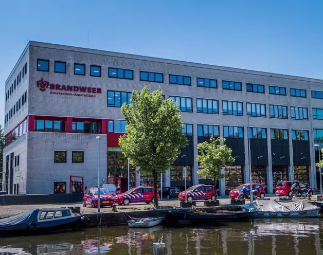 The headquarters of the Amsterdam-Amstelland Safety Region on a canal, with fire trucks and boats parked in front.