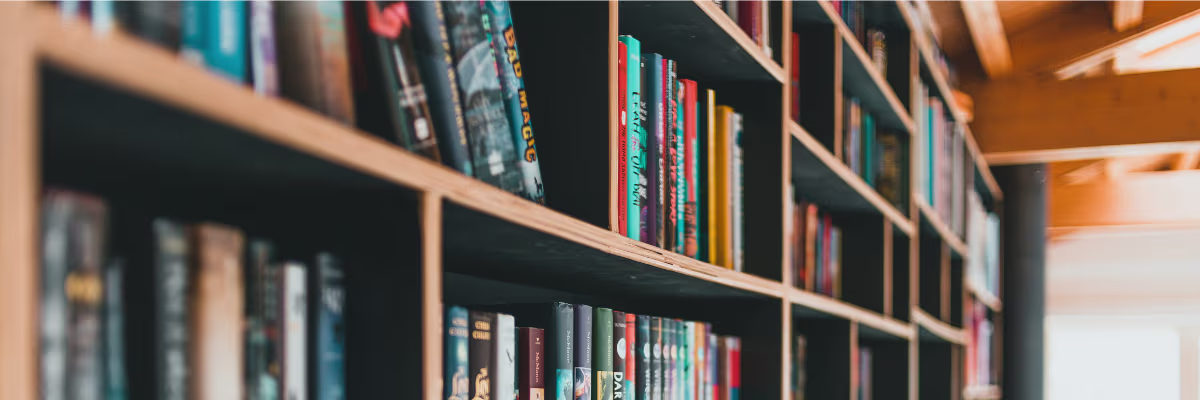 Boekenplanken vol met kleurrijke boeken in een bibliotheek, met warme verlichting op de achtergrond.