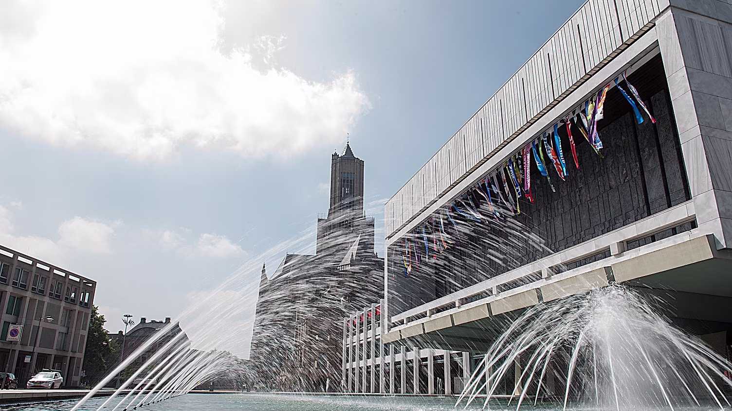 Modern gemeentehuis van Arnhem met fontein op voorgrond en kenmerkende toren op achtergrond onder blauwe hemel.