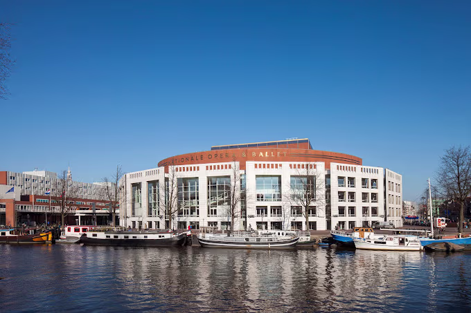 Het imposante gebouw van Nationale Opera & Ballet aan het water met boten ervoor onder een heldere blauwe hemel.