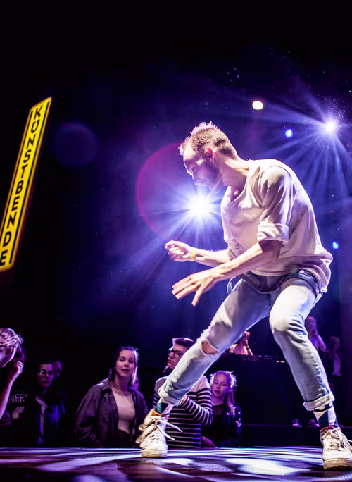 Een danser in actie op een podium met dramatische verlichting, omringd door een publiek dat geniet van de voorstelling.