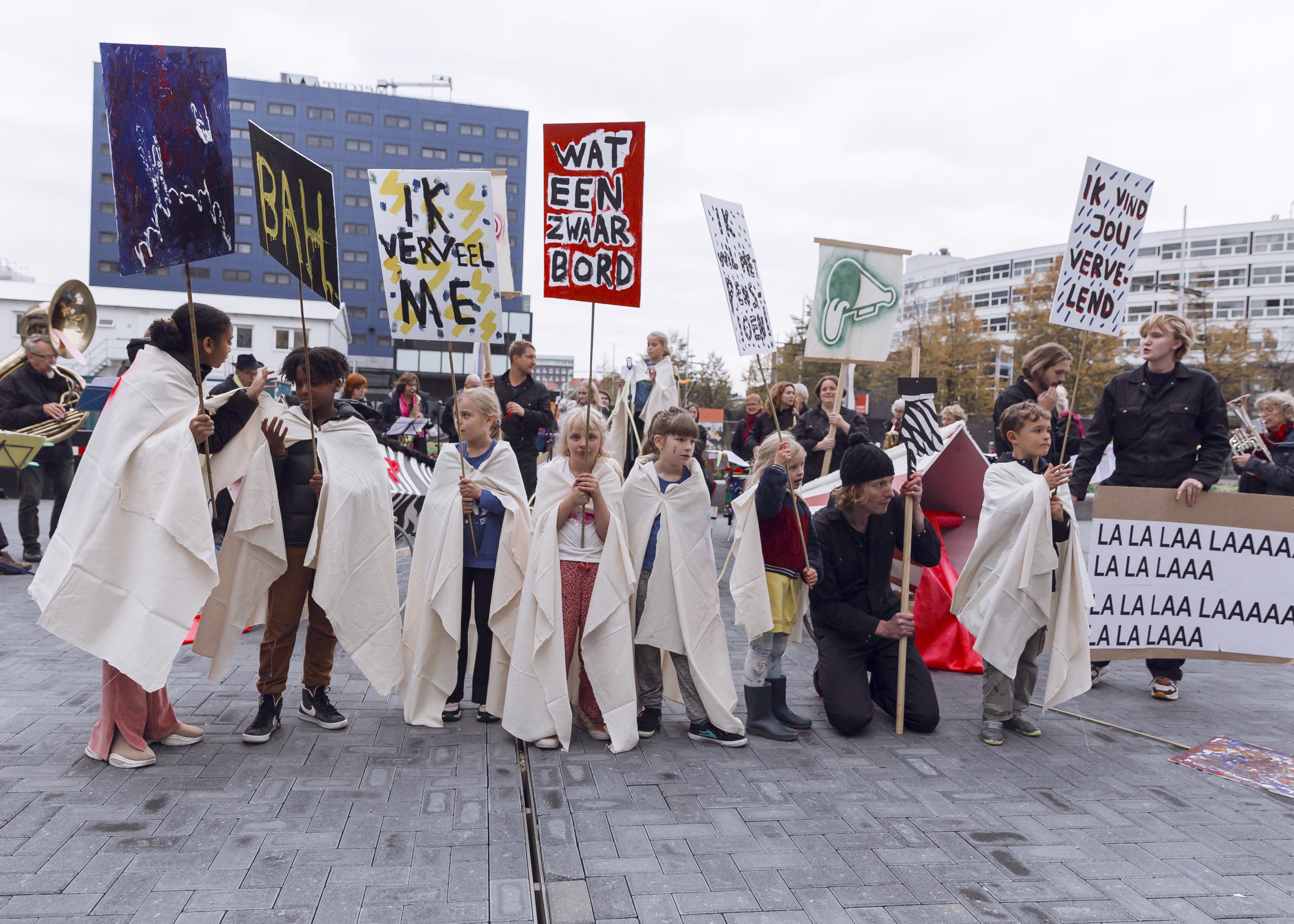 Groep kinderen in witte gewaden houdt protestborden vast tijdens een demonstratie op een stadsplein.