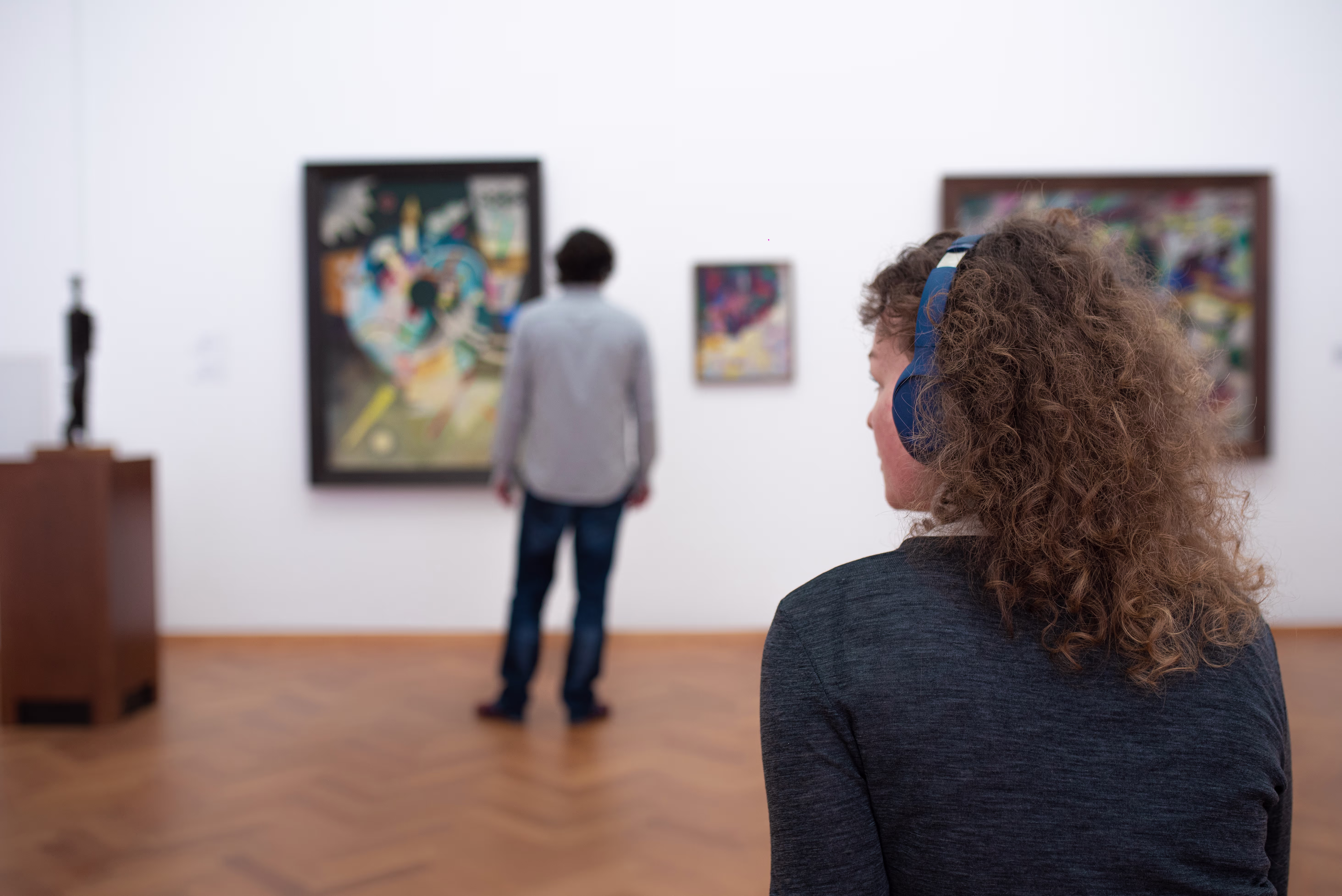 Bezoekers bekijken schilderijen in een museumzaal met witte muren en houten vloer.