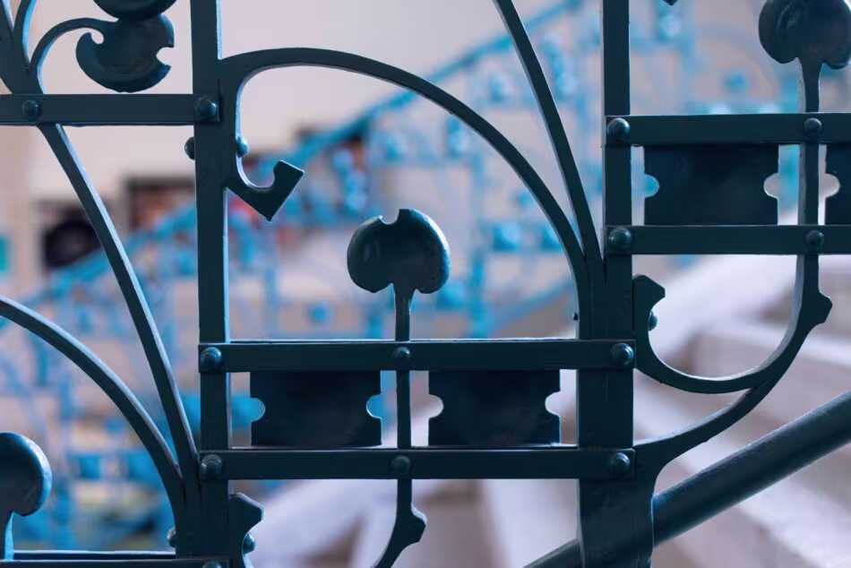 Close-up van decoratief smeedijzeren hekwerk met sierlijke krullen en geometrische patronen tegen een wazige achtergrond.