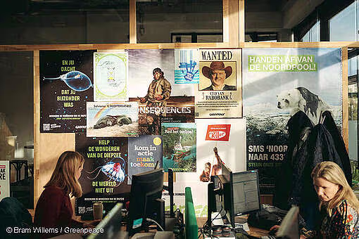 Twee medewerkers werken aan hun bureau voor een wand vol Greenpeace-campagneposters.