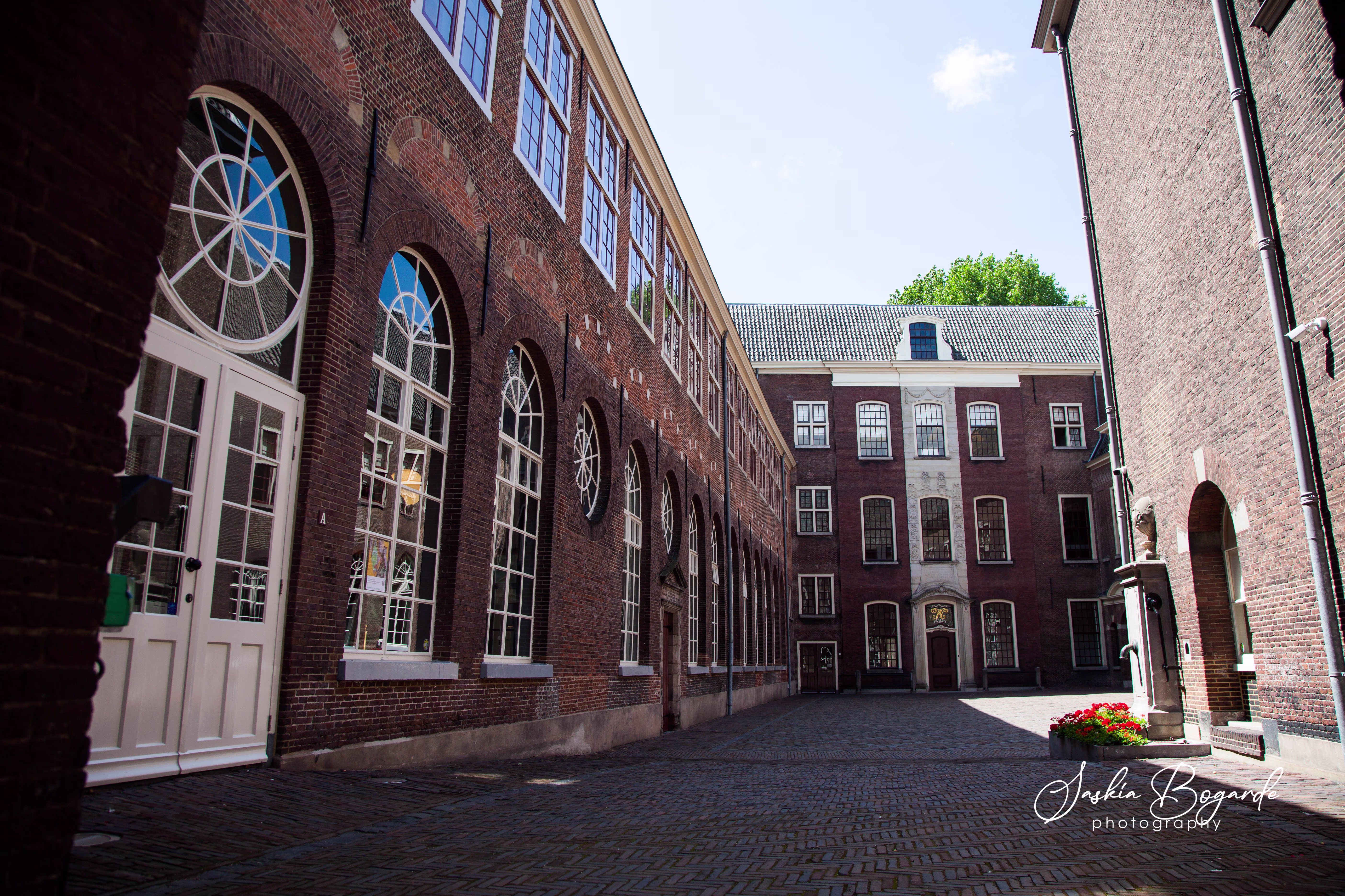 Historisch gebouw met bakstenen gevel en boogvensters rondom een rustige binnenplaats met kinderkopjes.
