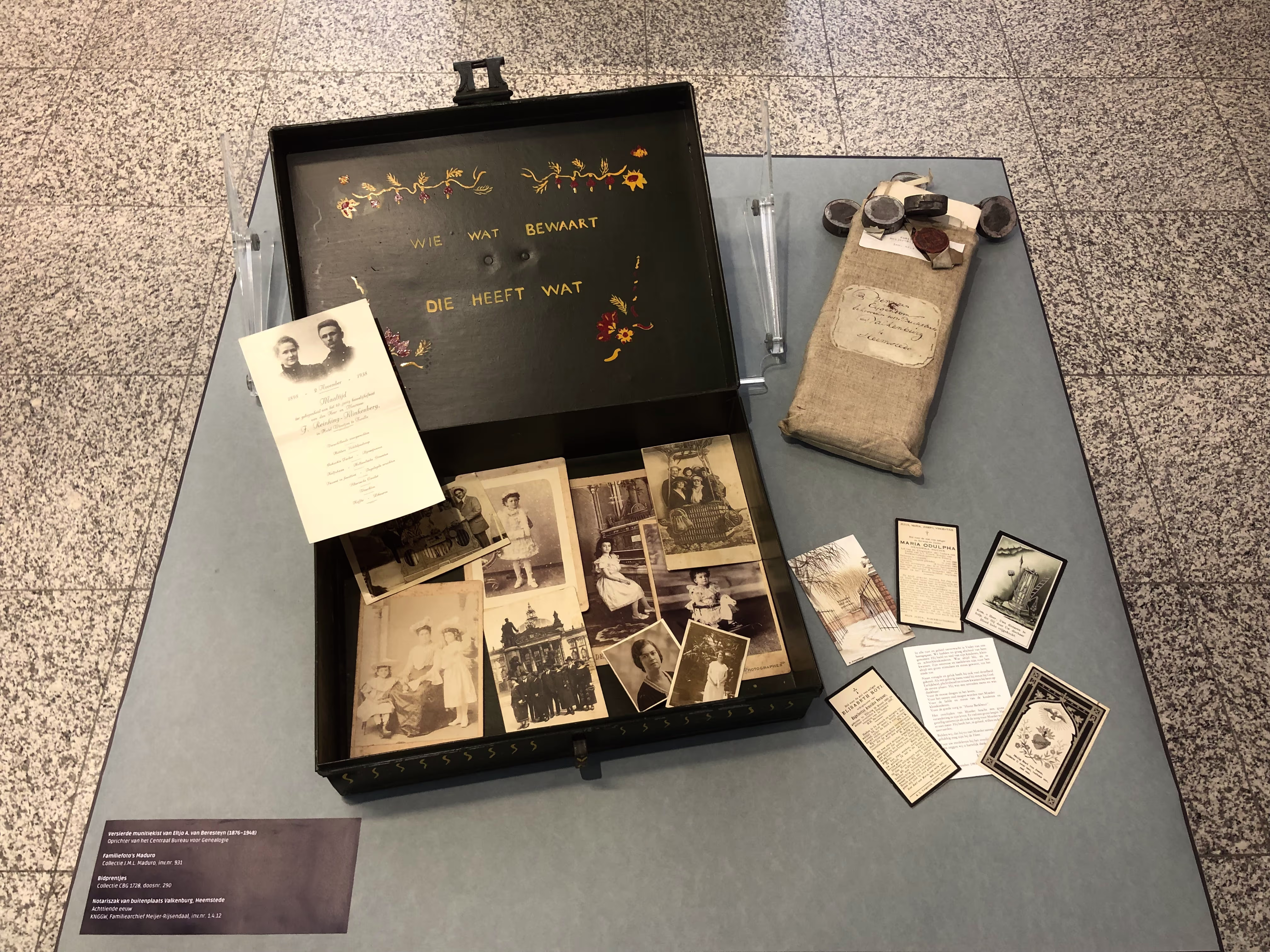 Museumopstelling met een vintage koffer gevuld met familieportretten, bidprentjes en documenten bij het CBG.